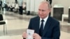 Russian President Vladimir Putin shows his passport to a member of an election commission as he arrives to take part in voting at a polling station in Moscow, Russia, July 1, 2020.