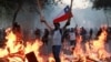 Un manifestante sostiene una bandera de Chile mientras está parado cerca de muebles en llamas durante una protesta contra el gobierno de Chile en Santiago, Chile, 18 de noviembre de 2019.