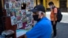Hombres, con máscaras faciales protectoras, se paran frente a un puesto de periódicos en el centro de Lima, Perú, el sábado 28 de marzo de 2020, durante la segunda semana de un estado de emergencia decretado por el gobierno.